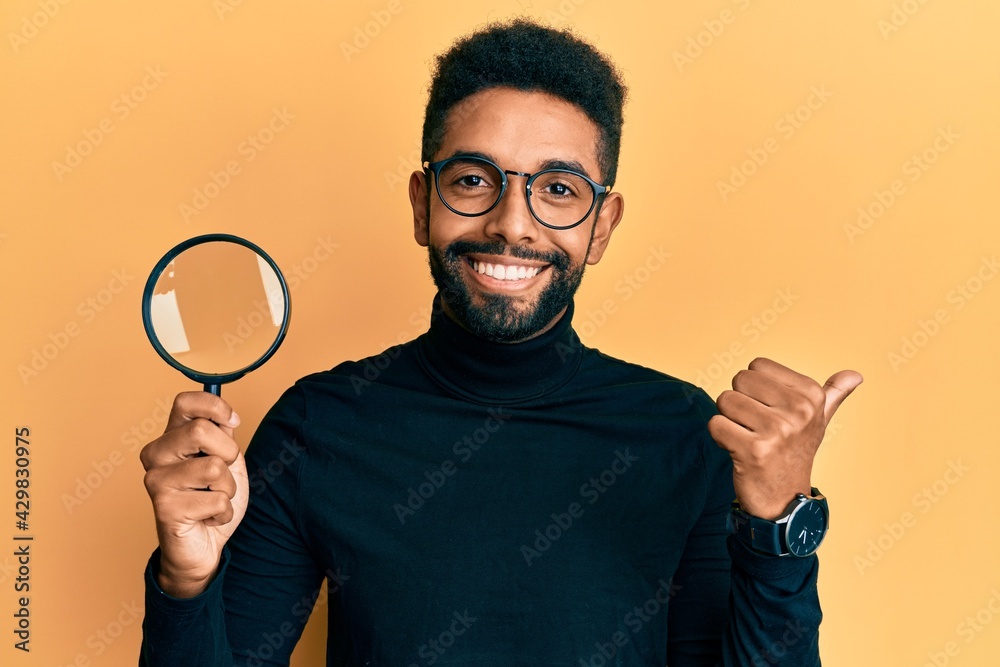 Handsome hispanic man with beard holding magnifying glass pointing thumb up to the side smiling happy with open mouth Handsome hispanic man with beard holding magnifying glass pointing thumb up to the side smiling happy with open mouth