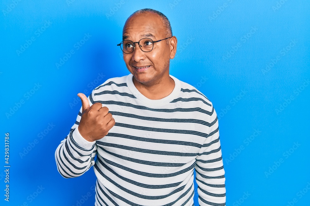 Naklejka premium Middle age latin man wearing casual clothes and glasses smiling with happy face looking and pointing to the side with thumb up.