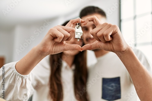 Young hispanic couple doing heart symbol with fingers and holding key of new home.