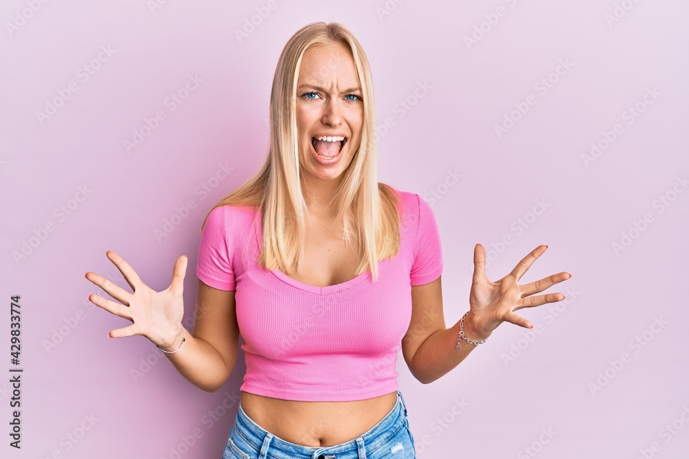 Young blonde girl wearing casual clothes crazy and mad shouting and yelling with aggressive expression and arms raised. frustration concept. Young blonde girl wearing casual clothes crazy and mad shouting and yelling with aggressive expression and arms raised. frustration concept.