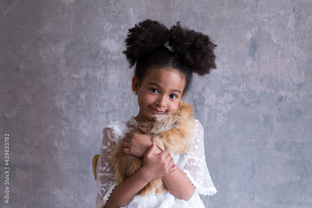 Medium shot of adorable mixed race little girl sitting in a lacy white dress holding a cute long-haired caramel rabbit tight to her chest Medium shot of adorable mixed race little girl sitting in a lacy white dress holding a cute long-haired caramel rabbit tight to her chest