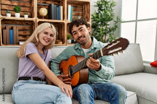Man playing spanish guitar to his girlfriend sitting on the sofa at home