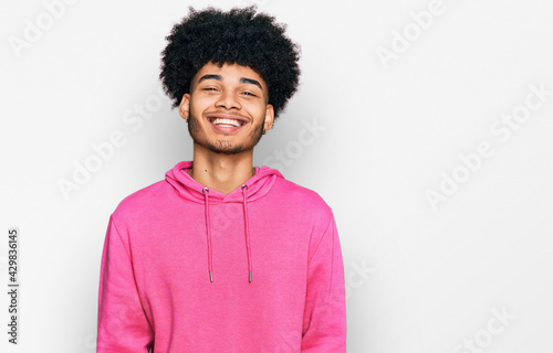 Young african american man with afro hair wearing casual pink sweatshirt with a happy and cool smile on face. lucky person.