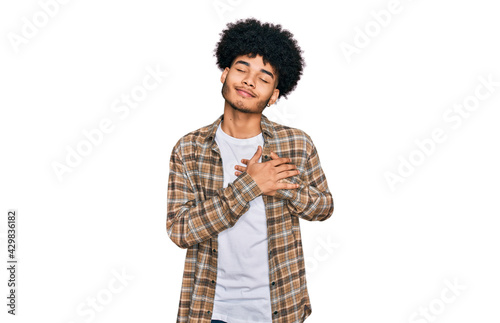 Young african american man with afro hair wearing casual clothes smiling with hands on chest with closed eyes and grateful gesture on face. health concept.