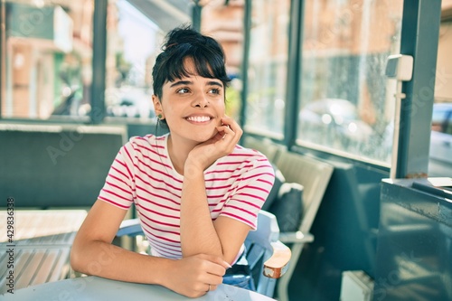 Young hispanic girl smiling happy sitting at the coffee shop terrace.
