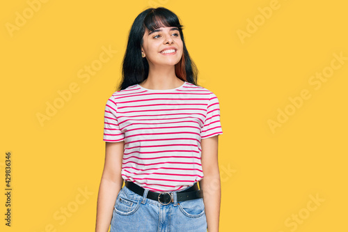 Young hispanic girl wearing casual clothes looking away to side with smile on face, natural expression. laughing confident.