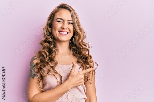 Young blonde girl wearing casual clothes cheerful with a smile of face pointing with hand and finger up to the side with happy and natural expression on face