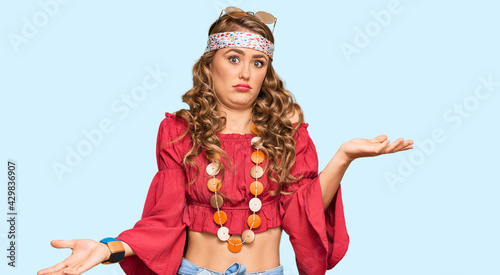 Young blonde girl wearing bohemian and hippie style clueless and confused expression with arms and hands raised. doubt concept.