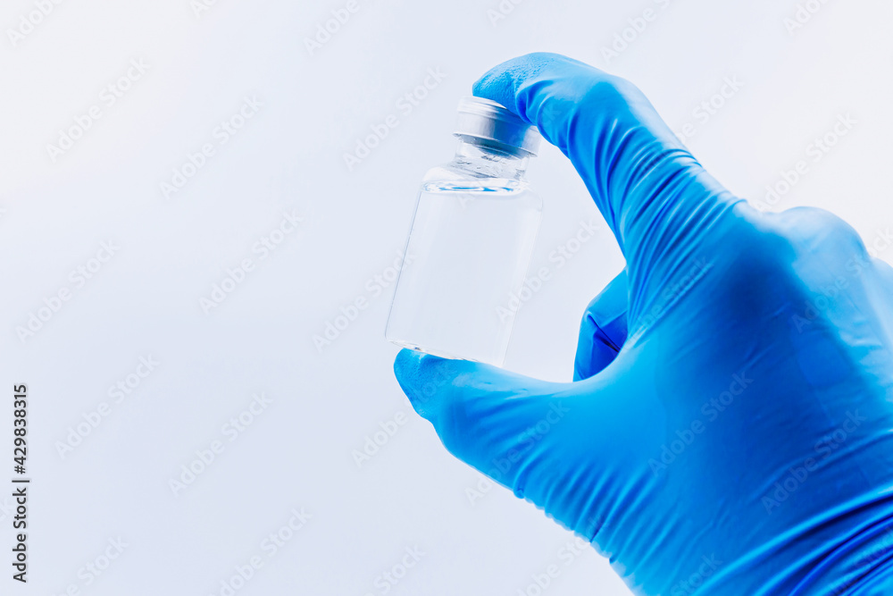 The vaccine concept is in the hands of a doctor's white vaccine bottle and a blue glove with copy space, isolated on black background