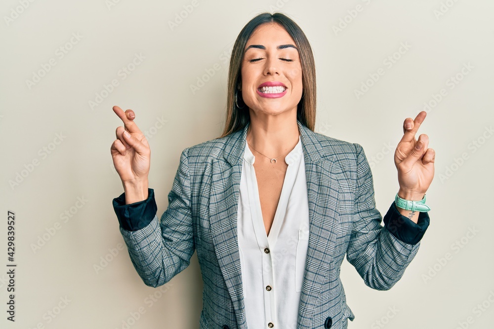 Young hispanic woman wearing business clothes gesturing finger crossed smiling with hope and eyes closed. luck and superstitious concept. Young hispanic woman wearing business clothes gesturing finger crossed smiling with hope and eyes closed. luck and superstitious concept.