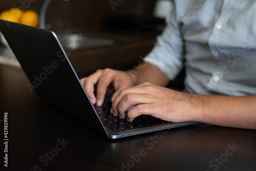 Man hands typing on laptop  sitting in a kitchen. Working at home