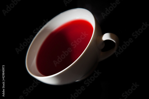 A white teacup with red berry tea. A black background