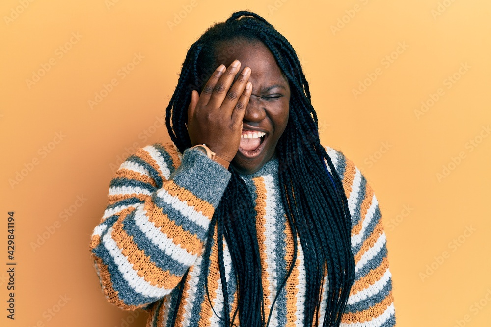 Young black woman with braids wearing casual winter sweater yawning tired covering half face, eye and mouth with hand. face hurts in pain. Young black woman with braids wearing casual winter sweater yawning tired covering half face, eye and mouth with hand. face hurts in pain.