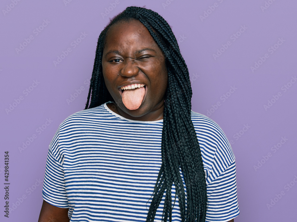 Young black woman with braids wearing casual clothes sticking tongue out happy with funny expression. emotion concept.