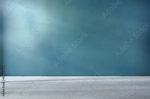 Teal textured wall and concrete floor in empty room for displaying your product, light coming through window, industrial atmosphere.