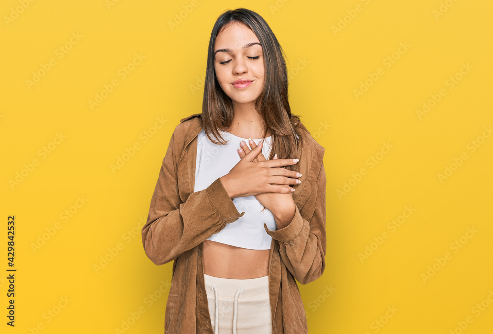 Young brunette woman wearing casual clothes smiling with hands on chest with closed eyes and grateful gesture on face. health concept. Young brunette woman wearing casual clothes smiling with hands on chest with closed eyes and grateful gesture on face. health concept.