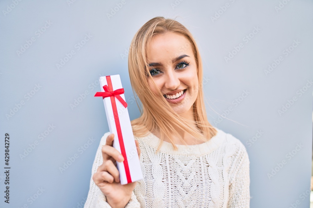Young blonde girl smiling happy holding gift standing at the city. Young blonde girl smiling happy holding gift standing at the city.