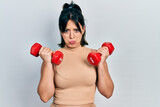 Young hispanic woman wearing sportswear using dumbbells depressed and worry for distress, crying angry and afraid. sad expression.