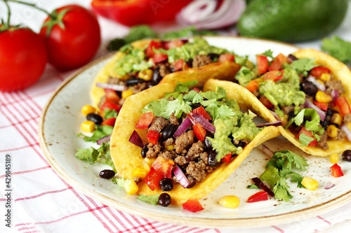 Mexican tacos with roast minced meat with corn and black beans, onions, fresh tomatoes, paprika and cilantro are flavored with guacamole sauce.