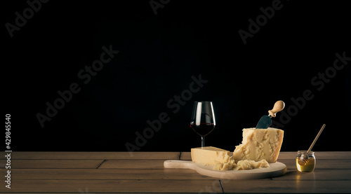 Tavola imbandita con due bicchieri di vino rosso, formaggio parmigiano reggiano su un tagliere con coltello e miele in un contenitore di vetro con dosatore. photo