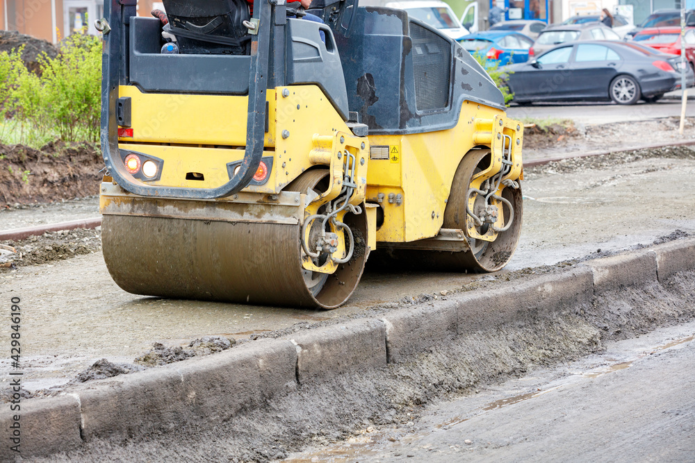 The compact road roller ramps the pavement foundation along the concrete curb and driveway.