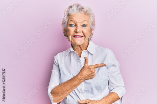 Senior grey-haired woman wearing casual clothes smiling cheerful pointing with hand and finger up to the side