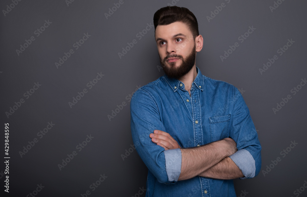 Confident serious hipster modern bearded man in jeans shirt with crossed arms is posing and looking right on the camera.