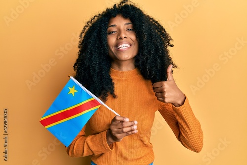 African american woman with afro hair holding democratic republic of the congo flag smiling happy and positive, thumb up doing excellent and approval sign