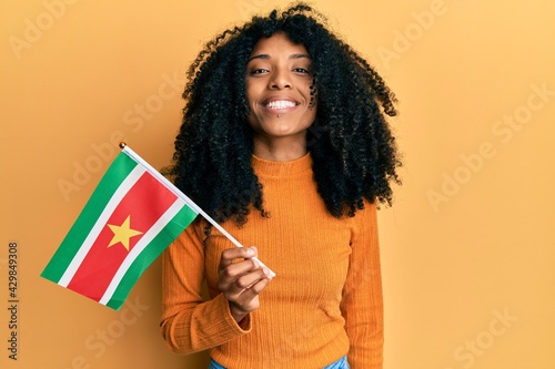 African american woman with afro hair holding suriname flag looking positive and happy standing and smiling with a confident smile showing teeth
