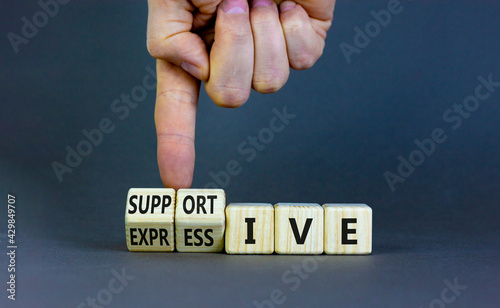 Supportive or expressive symbol. Businessman turns cubes and changes words 'supportive' to 'expressive'. Beautiful grey background, copy space. Business, supportive or expressive concept.