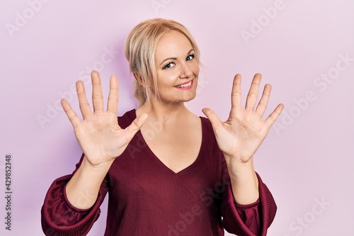 Young blonde woman wearing casual winter sweater showing and pointing up with fingers number ten while smiling confident and happy.