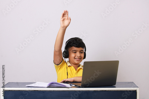 Happy indian school pupil or boy wearing headphones raising hand distance learning online at virtual lesson class photo