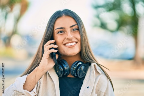 Young hispanic girl smiling happy talking on the smartphone and using headphones at the city.