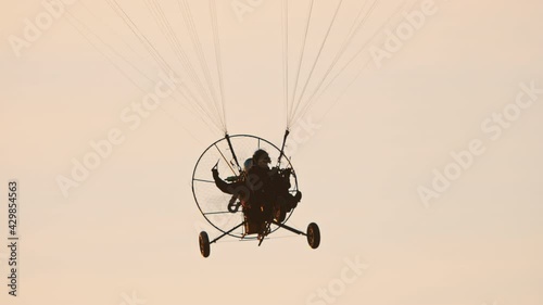 Close-up of paramotor trike under parachute flying towards camera, against sunset sky view. Tandem motor powered paragliding at twilight.  photo