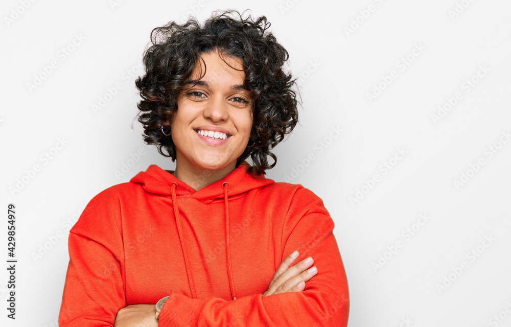 Young hispanic woman with curly hair wearing casual sweatshirt happy face smiling with crossed arms looking at the camera. positive person. Young hispanic woman with curly hair wearing casual sweatshirt happy face smiling with crossed arms looking at the camera. positive person.
