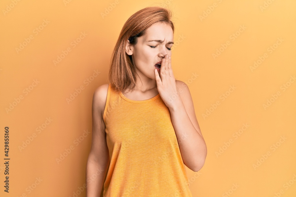 Young caucasian woman wearing casual style with sleeveless shirt bored yawning tired covering mouth with hand. restless and sleepiness. Young caucasian woman wearing casual style with sleeveless shirt bored yawning tired covering mouth with hand. restless and sleepiness.
