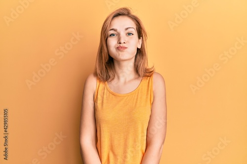 Young caucasian woman wearing casual style with sleeveless shirt puffing cheeks with funny face. mouth inflated with air, crazy expression.