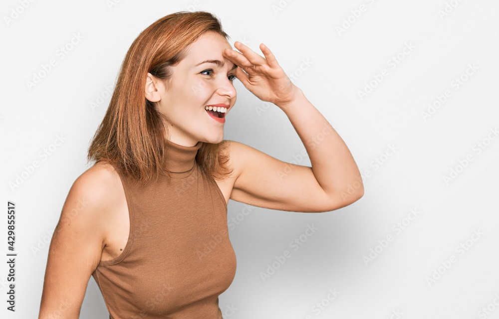 Young caucasian woman wearing casual clothes very happy and smiling looking far away with hand over head. searching concept. Young caucasian woman wearing casual clothes very happy and smiling looking far away with hand over head. searching concept.
