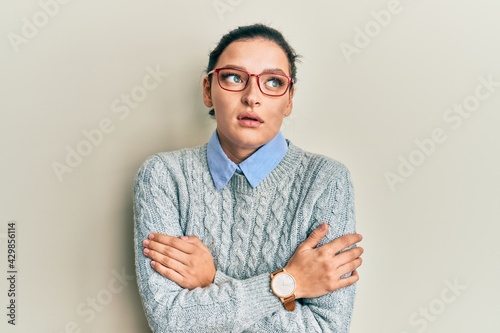 Young caucasian woman wearing casual clothes and glasses shaking and freezing for winter cold with sad and shock expression on face