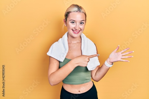 Young blonde girl wearing sportswear and towel amazed and smiling to the camera while presenting with hand and pointing with finger. © Krakenimages.com