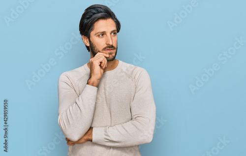 Young hispanic man wearing casual clothes serious face thinking about question with hand on chin, thoughtful about confusing idea