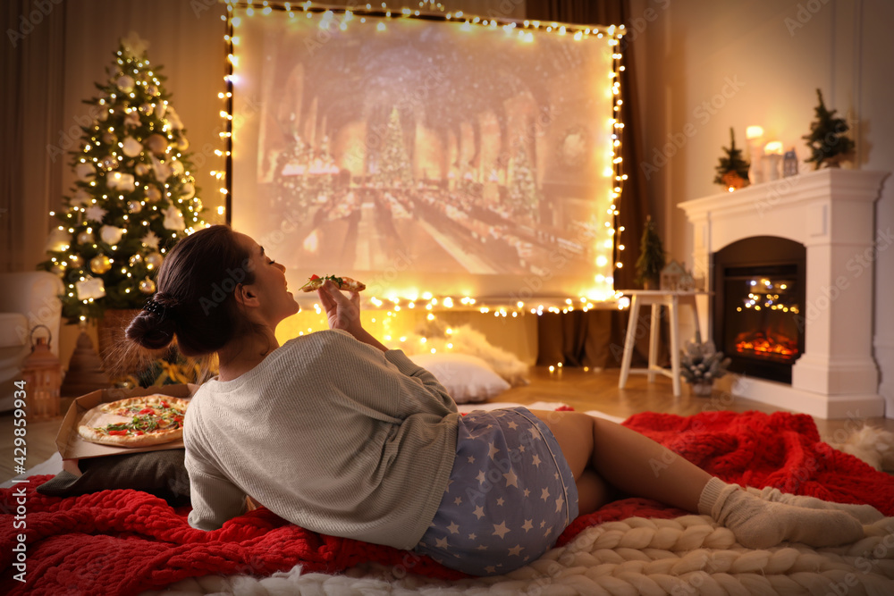 MYKOLAIV, UKRAINE - DECEMBER 24, 2020: Woman watching Harry Potter and Philosopher's Stone movie via video projector in room. Cozy winter holidays atmosphere - obrazy, fototapety, plakaty 