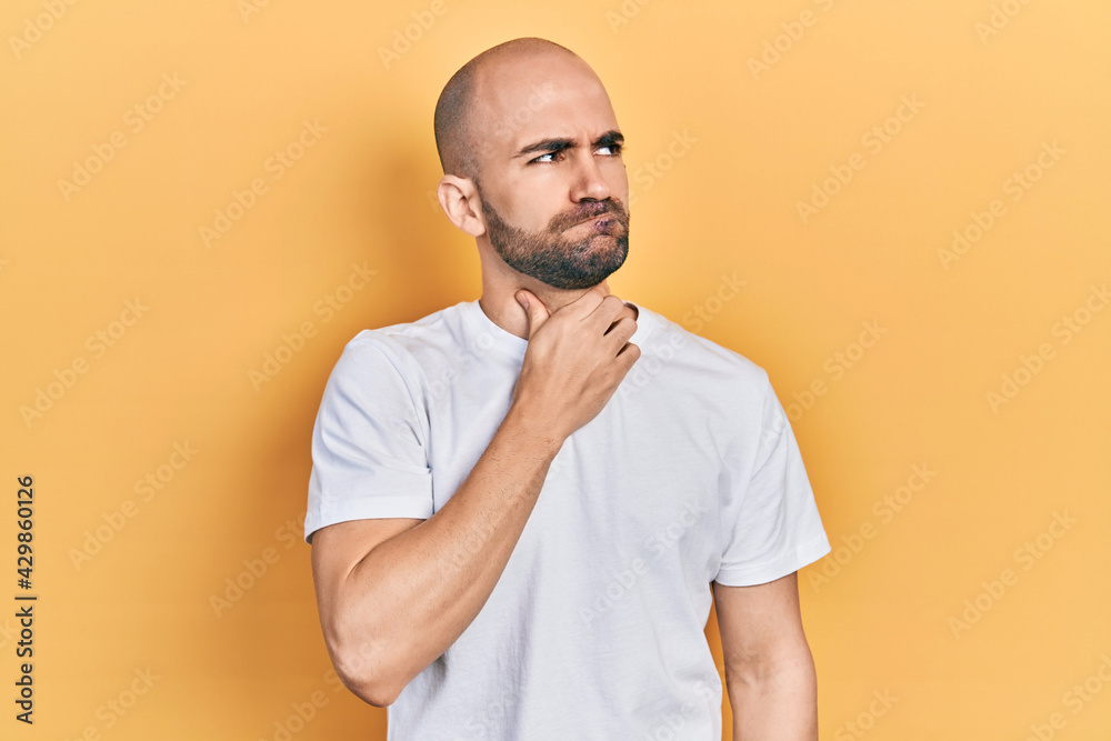 Young bald man wearing casual white t shirt touching painful neck, sore throat for flu, clod and infection Young bald man wearing casual white t shirt touching painful neck, sore throat for flu, clod and infection