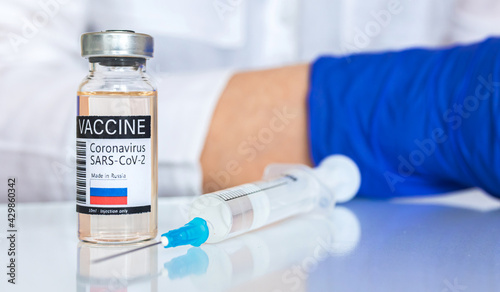 Vaccine vial with Russian flag on the label close-up, hospital background with doctor hands and medical syringe