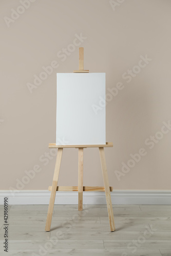 Fotografia Wooden easel with blank canvas near beige wall