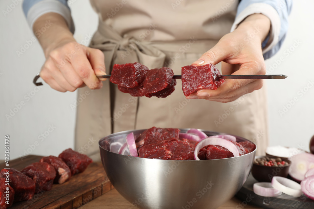 Woman stringing marinated meat on skewer at wooden table, closeup Woman stringing marinated meat on skewer at wooden table, closeup