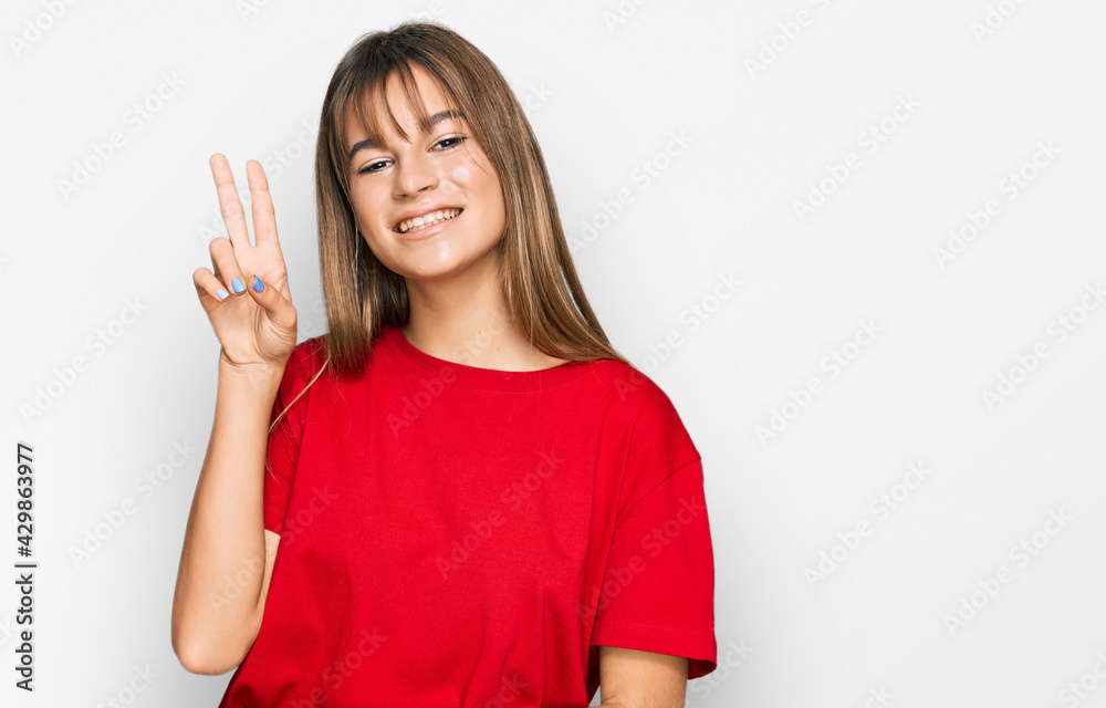 Teenager caucasian girl wearing casual red t shirt smiling with happy face winking at the camera doing victory sign with fingers. number two. Teenager caucasian girl wearing casual red t shirt smiling with happy face winking at the camera doing victory sign with fingers. number two.