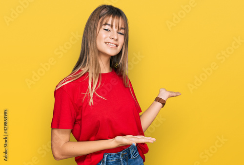 Teenager caucasian girl wearing casual red t shirt inviting to enter smiling natural with open hand