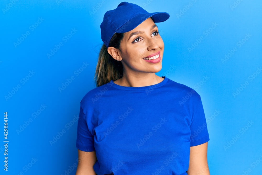 Beautiful brunette woman wearing delivery uniform looking away to side with smile on face, natural expression. laughing confident.