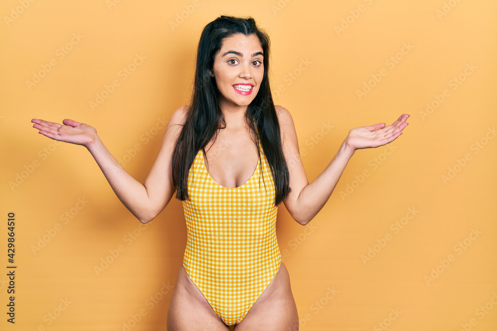 Young hispanic girl wearing swimsuit smiling showing both hands open palms, presenting and advertising comparison and balance Young hispanic girl wearing swimsuit smiling showing both hands open palms, presenting and advertising comparison and balance